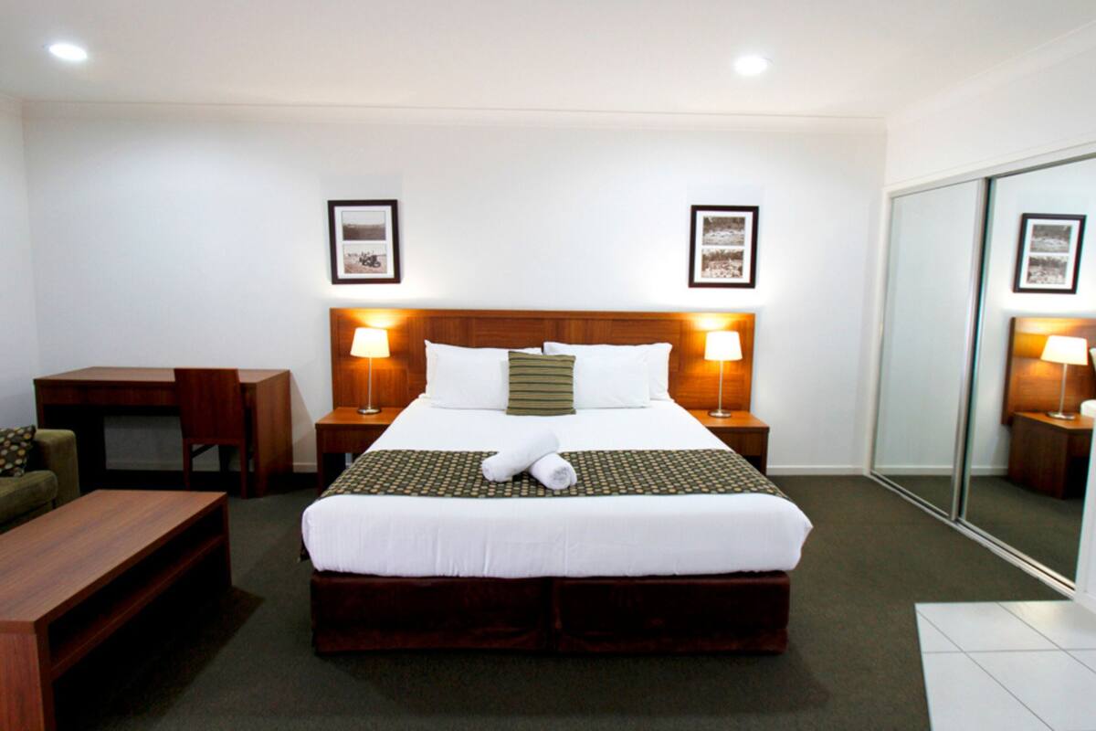 A neatly arranged hotel room with a large bed, two bedside tables with lamps, a wooden desk, a chair, and a mirror on the wall.