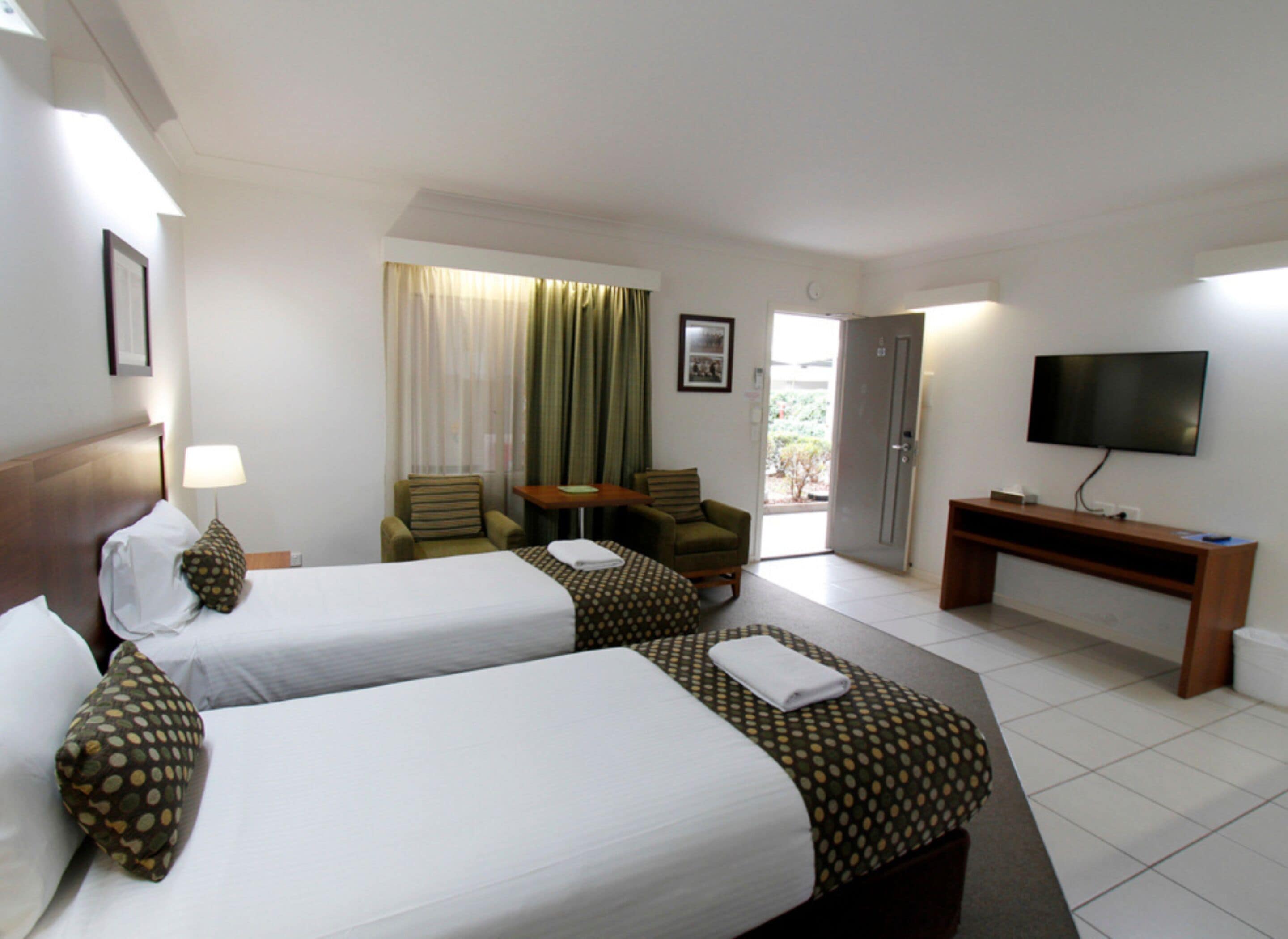 A hotel room with two beds, a desk, a TV, and a door leading outside.
