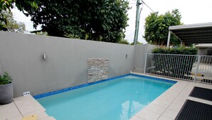 A rectangular swimming pool with a tiled deck, a stone accent wall, and a metal fence.