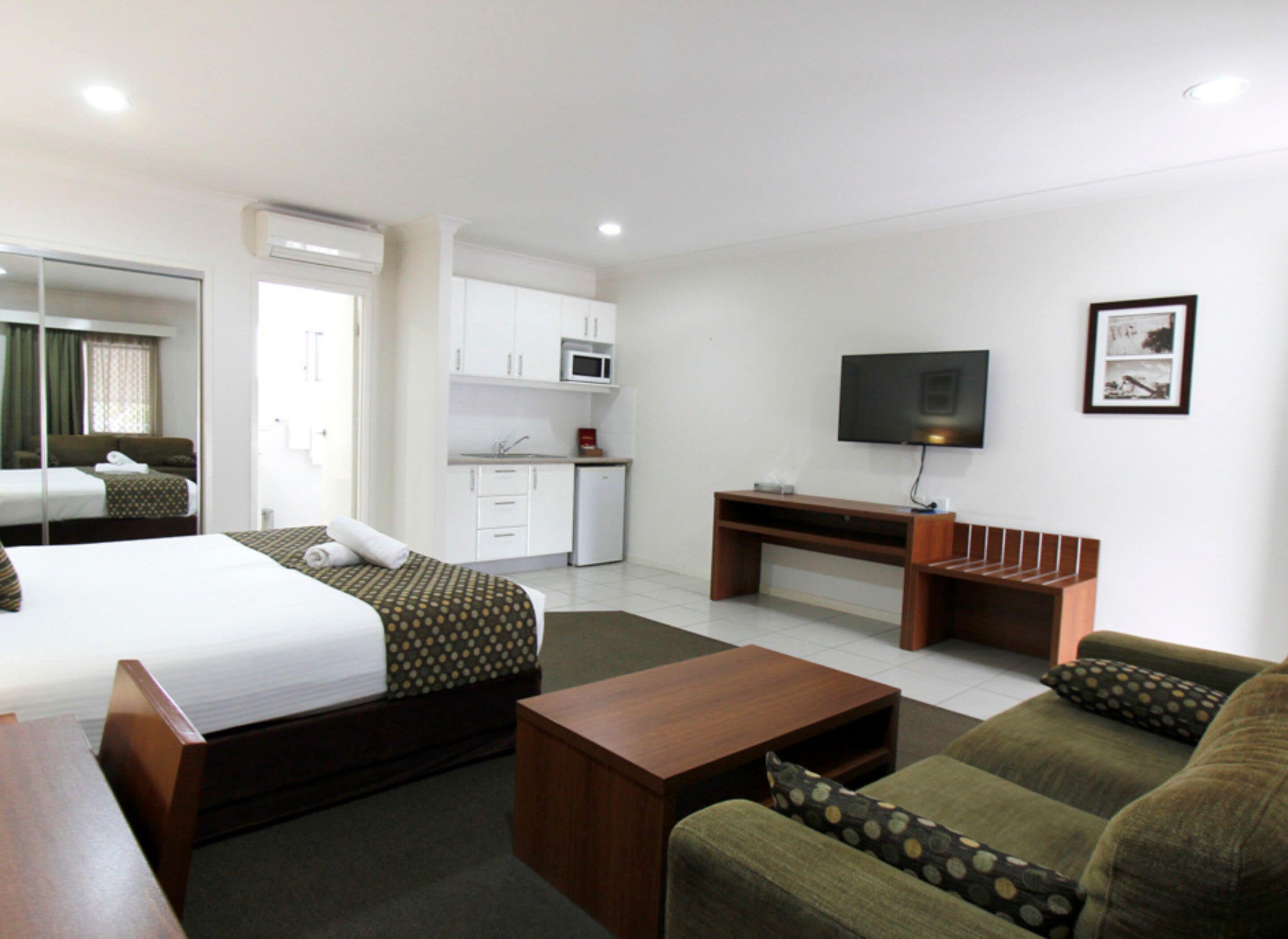 A hotel room with a bed, a sofa, a coffee table, a TV, a desk, and a kitchenette.