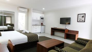 A hotel room with a bed, a sofa, a coffee table, a TV, a desk, and a kitchenette.