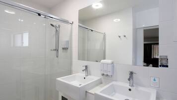Un baño moderno con ducha envuelta en vidrio, dos lavamanos blancos y un espejo grande.