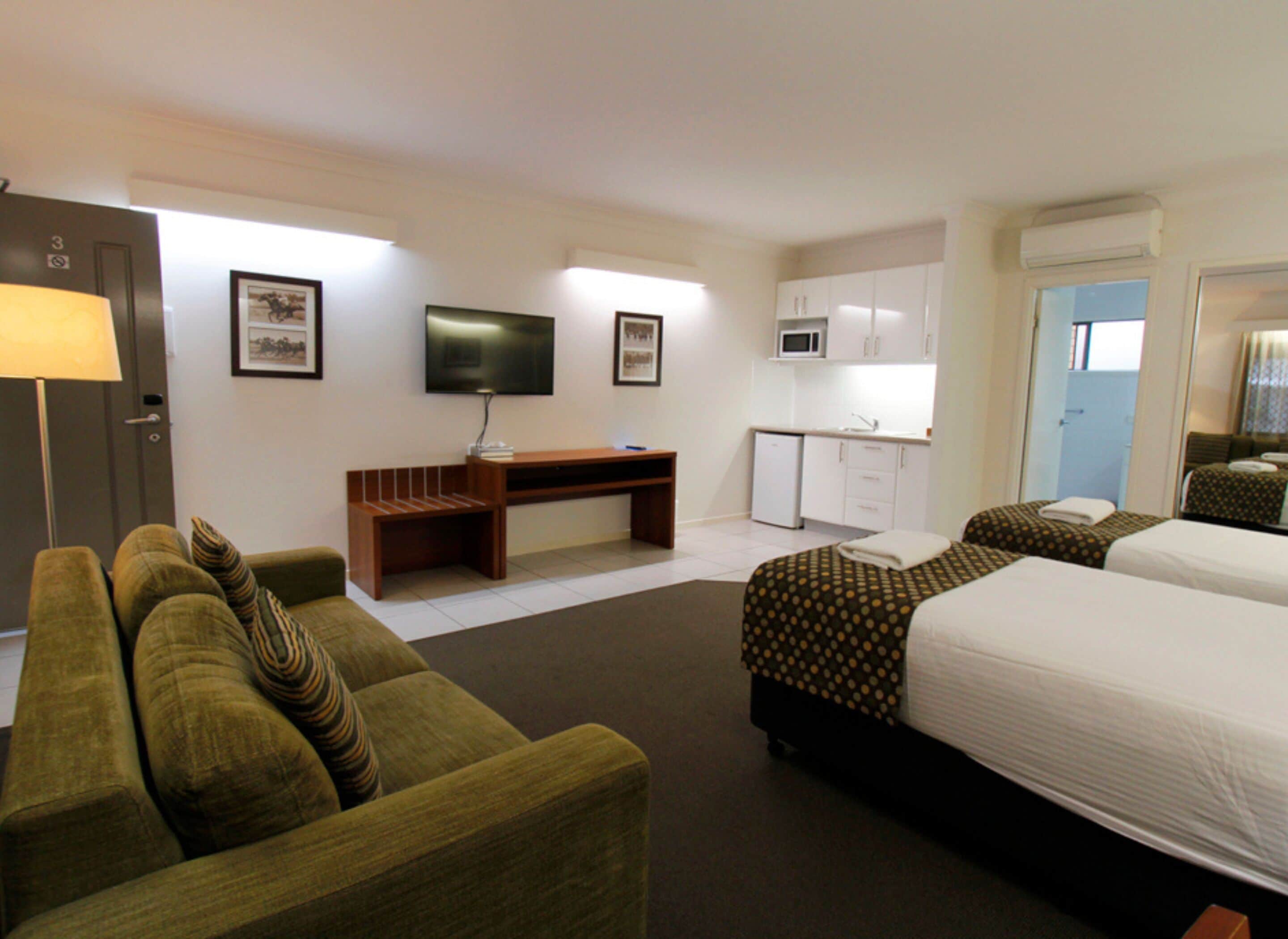 A hotel room with a sofa, a desk, a television, a bed, and a kitchenette.