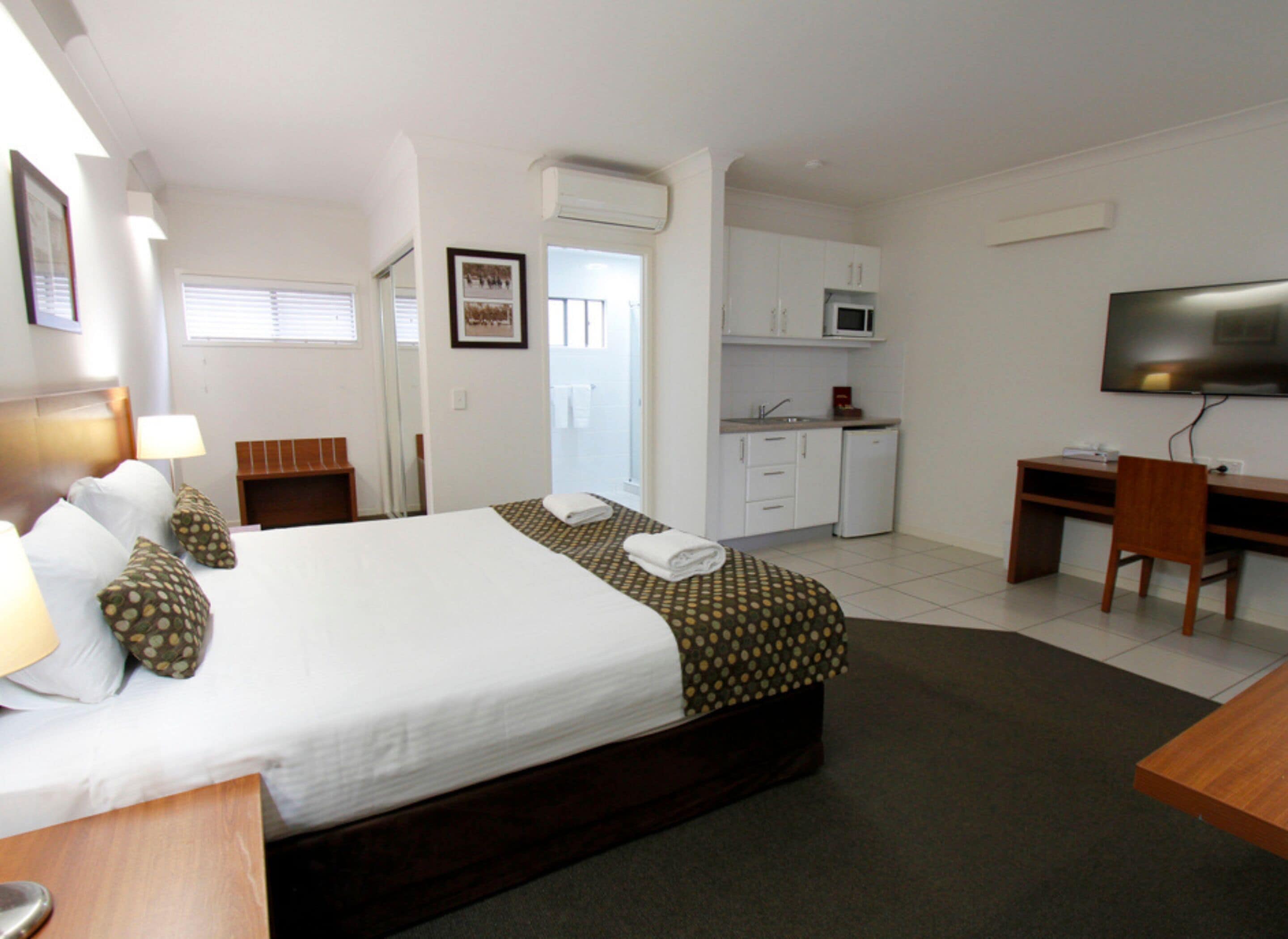 Habitación de hotel con cama, escritorio, televisor, microondas y pequeña cocina.