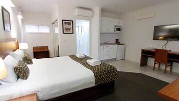 Habitación de hotel con cama, escritorio, televisor, microondas y pequeña cocina.