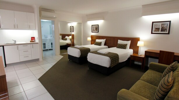 A hotel room with two beds, a sofa, a desk, and a kitchenette.
