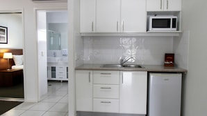 A compact kitchen with white cabinets, a microwave, a sink, and a small refrigerator.