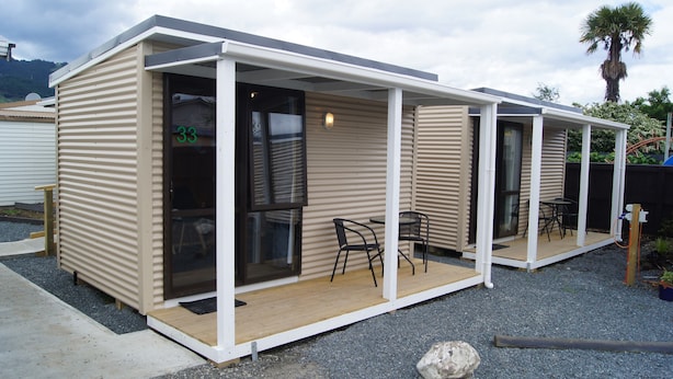 A modern, single-story mobile home with a covered patio area, two chairs, and a small table.