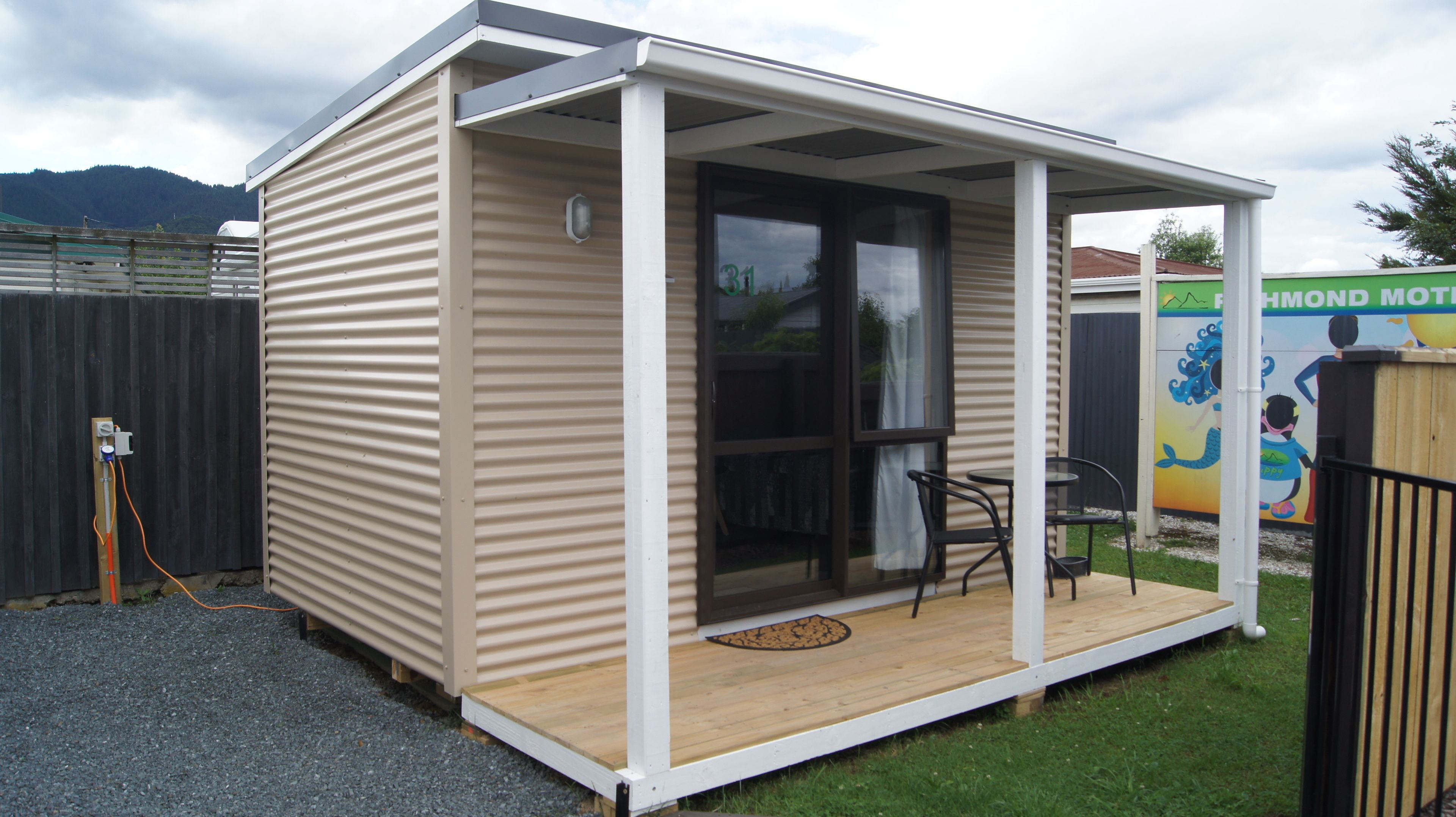 A small, single-story building with a covered porch, a sliding glass door, and a small outdoor seating area.