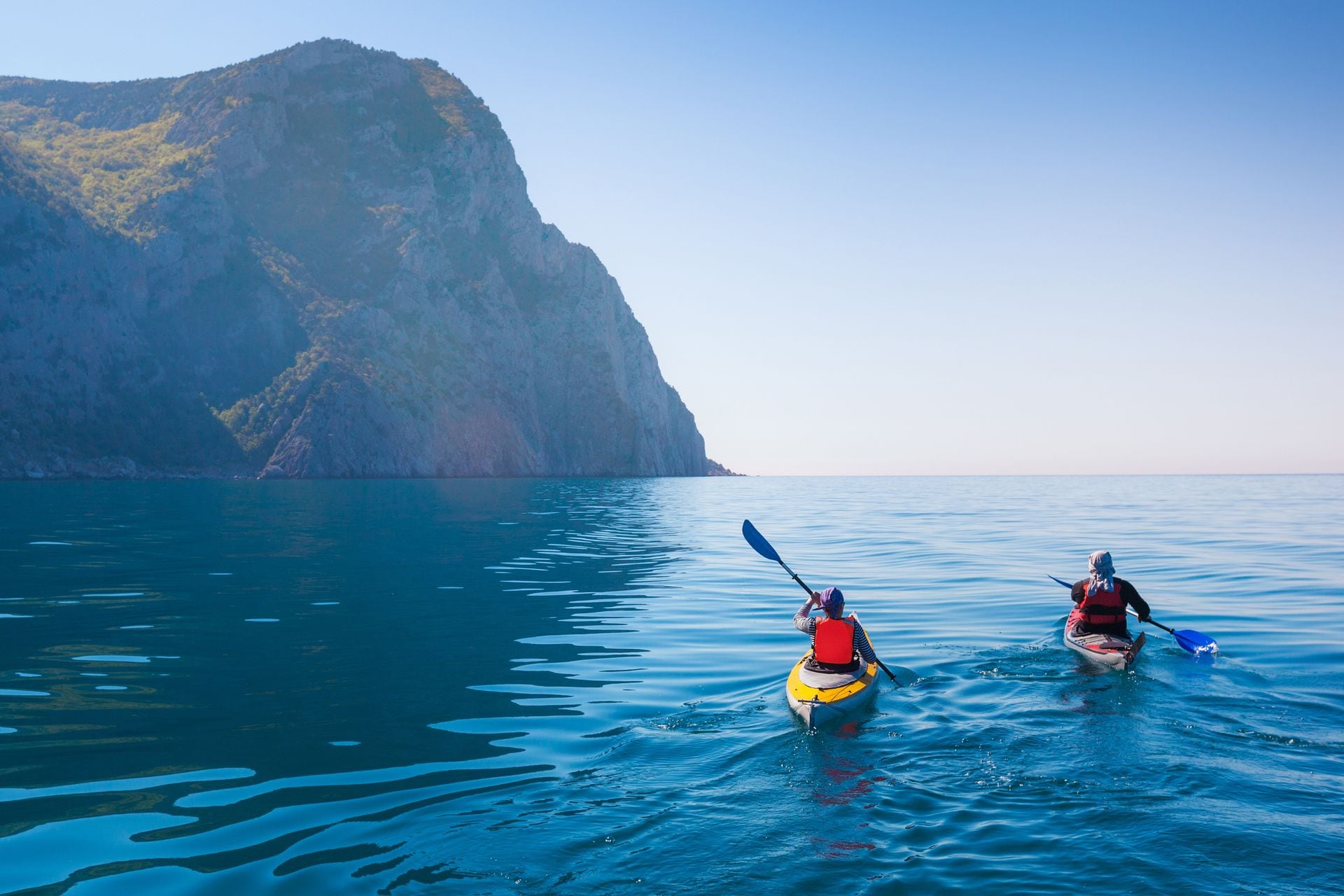 Two kayakers on a calm sea with a mountainous backdrop.