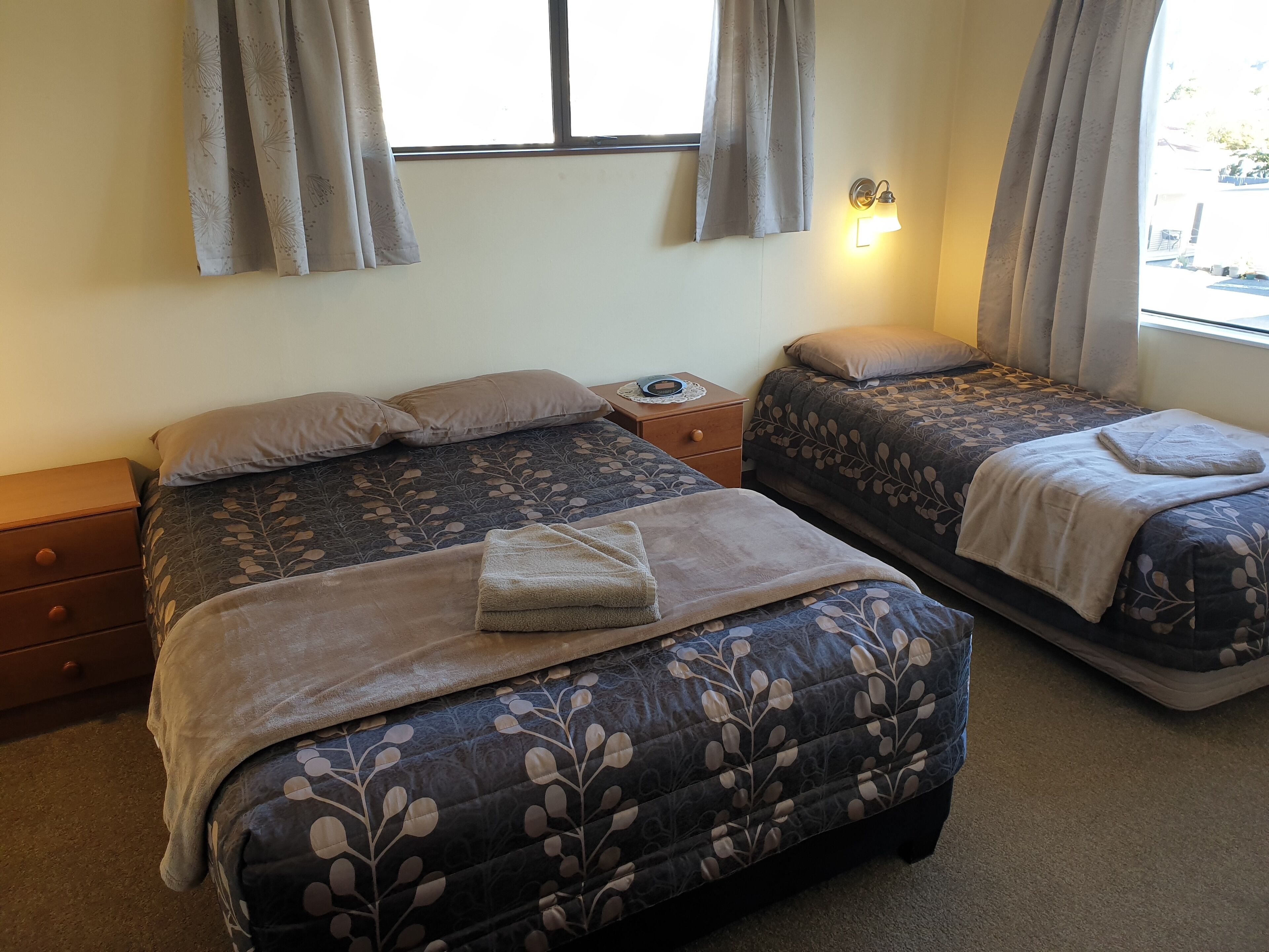 A bedroom with two beds, a nightstand, and a window with curtains.