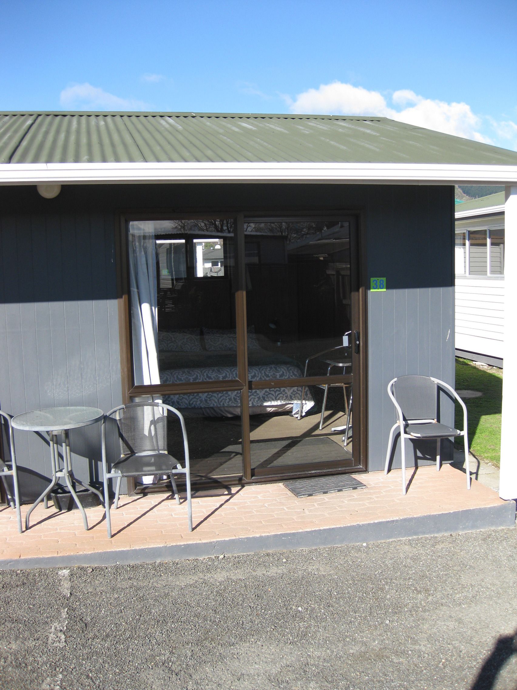 A small outdoor seating area with two tables and two chairs, a sliding glass door entrance, and a metal roof.