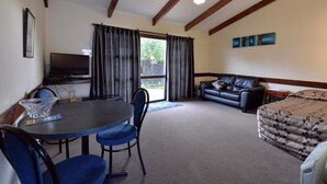 A room with a dining table, chairs, a sofa, a bed, a TV, and a window with curtains.