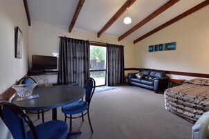 Quarto com mesa de jantar, cadeiras, sofá, cama, televisão e janela com cortinas.