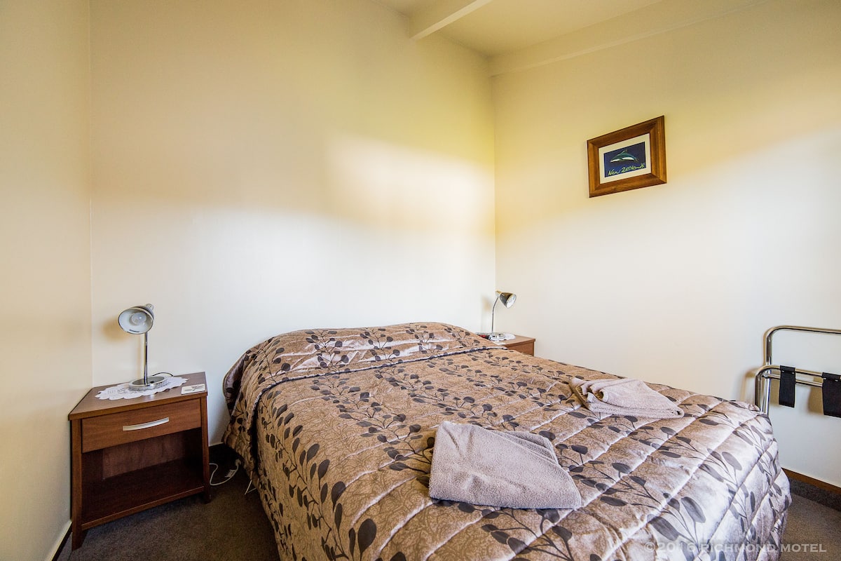 Une chambre à coucher avec un lit, une table de chevet, une lampe, un tableau au mur et une serviette sur le lit.
