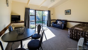 A room with a dining table, chairs, a sofa, a bed, a TV, and a large window with curtains.
