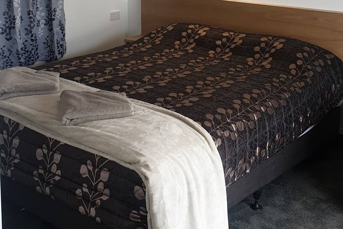 Un lit bien fait, recouvert d’une couvre-lit à motifs, avec une suspension au plafond et une applique murale.