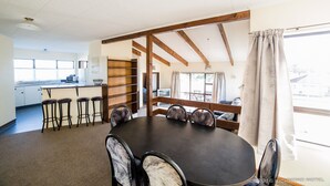 A dining area with a round table, bar stools, and a view of the kitchen and outside.