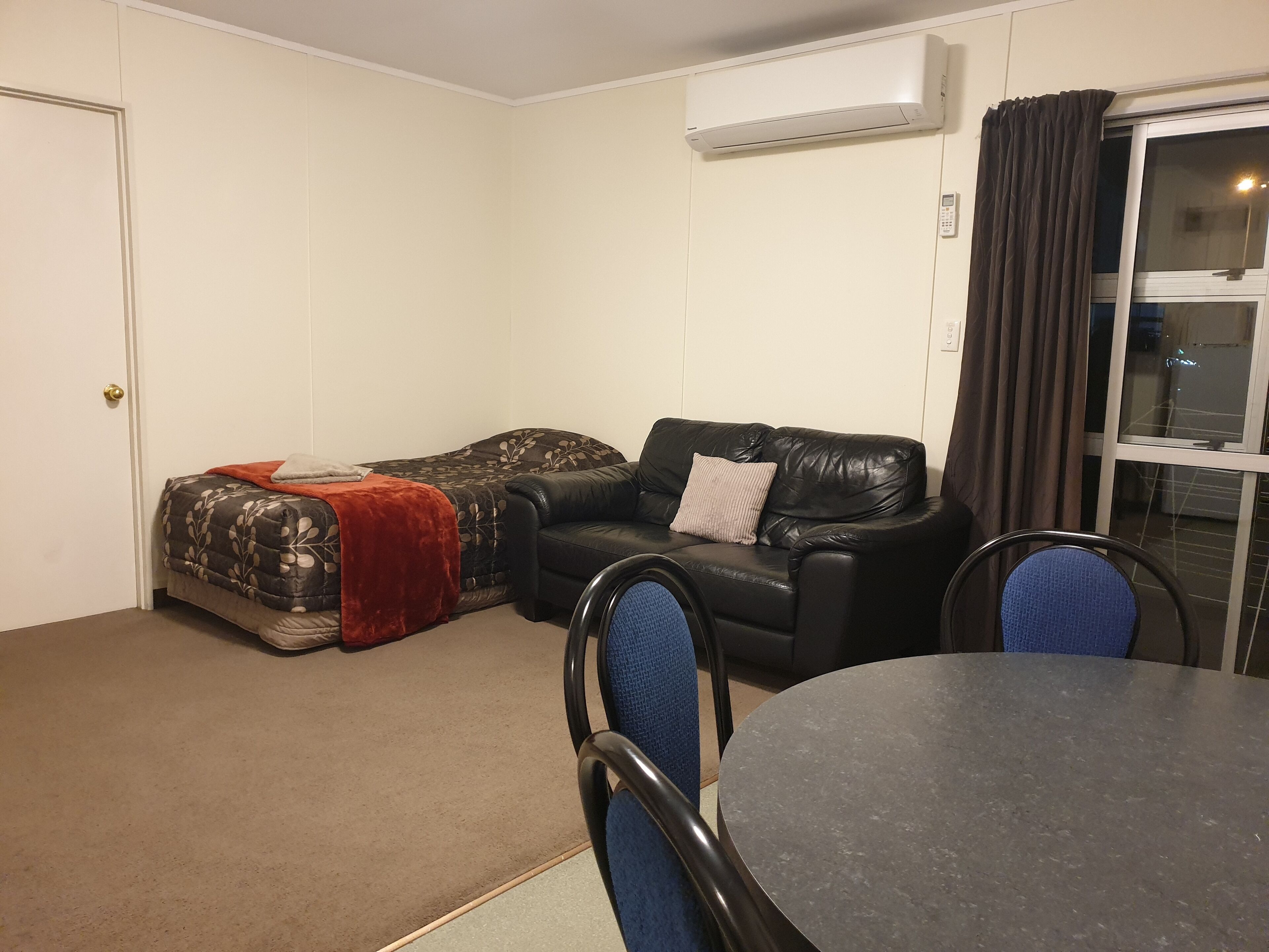 Quarto com cama, sofá de couro preto, mesa de jantar e aparelho de ar condicionado.