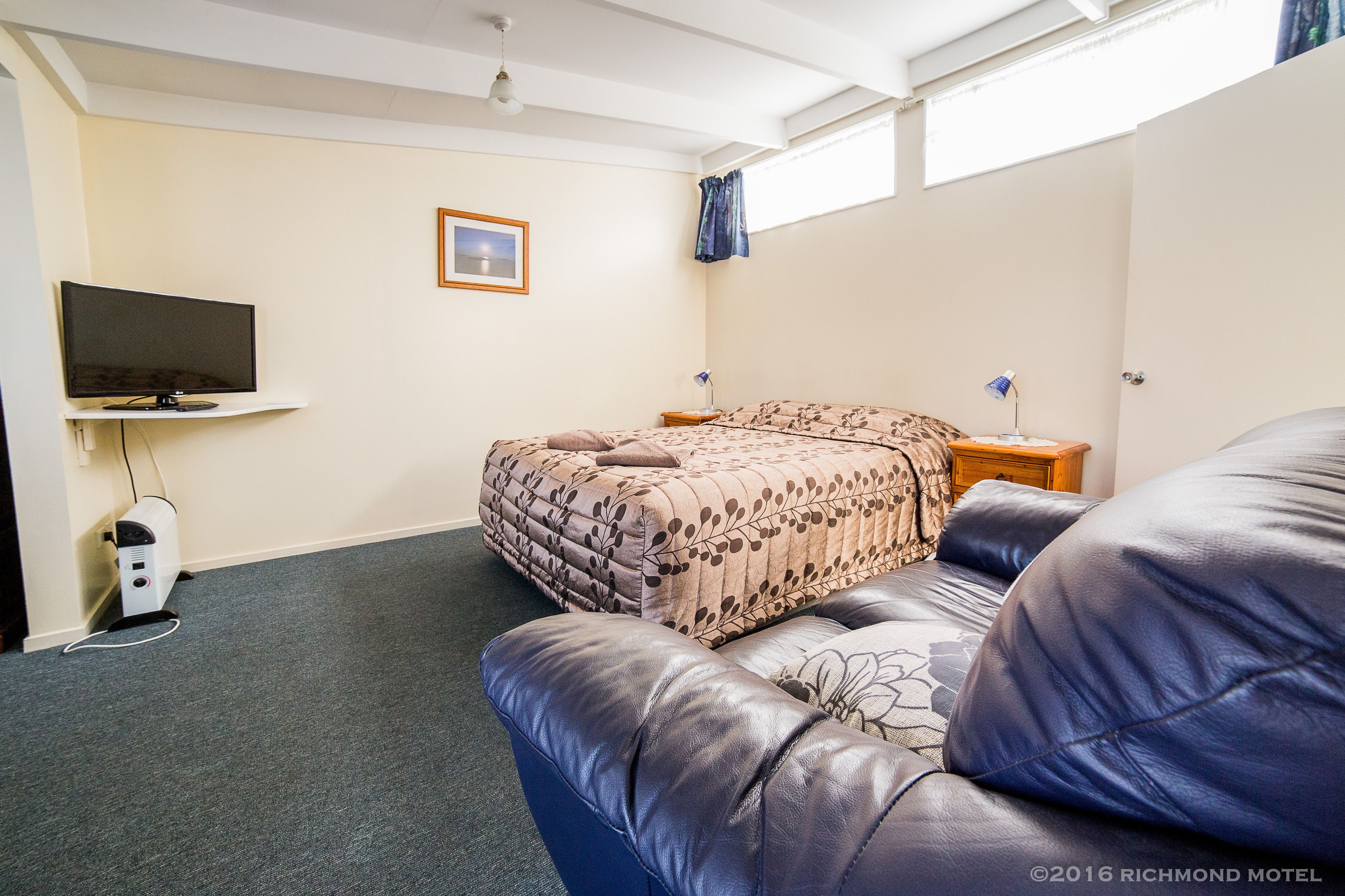 A room with a bed, a television, a desk, and a chair.