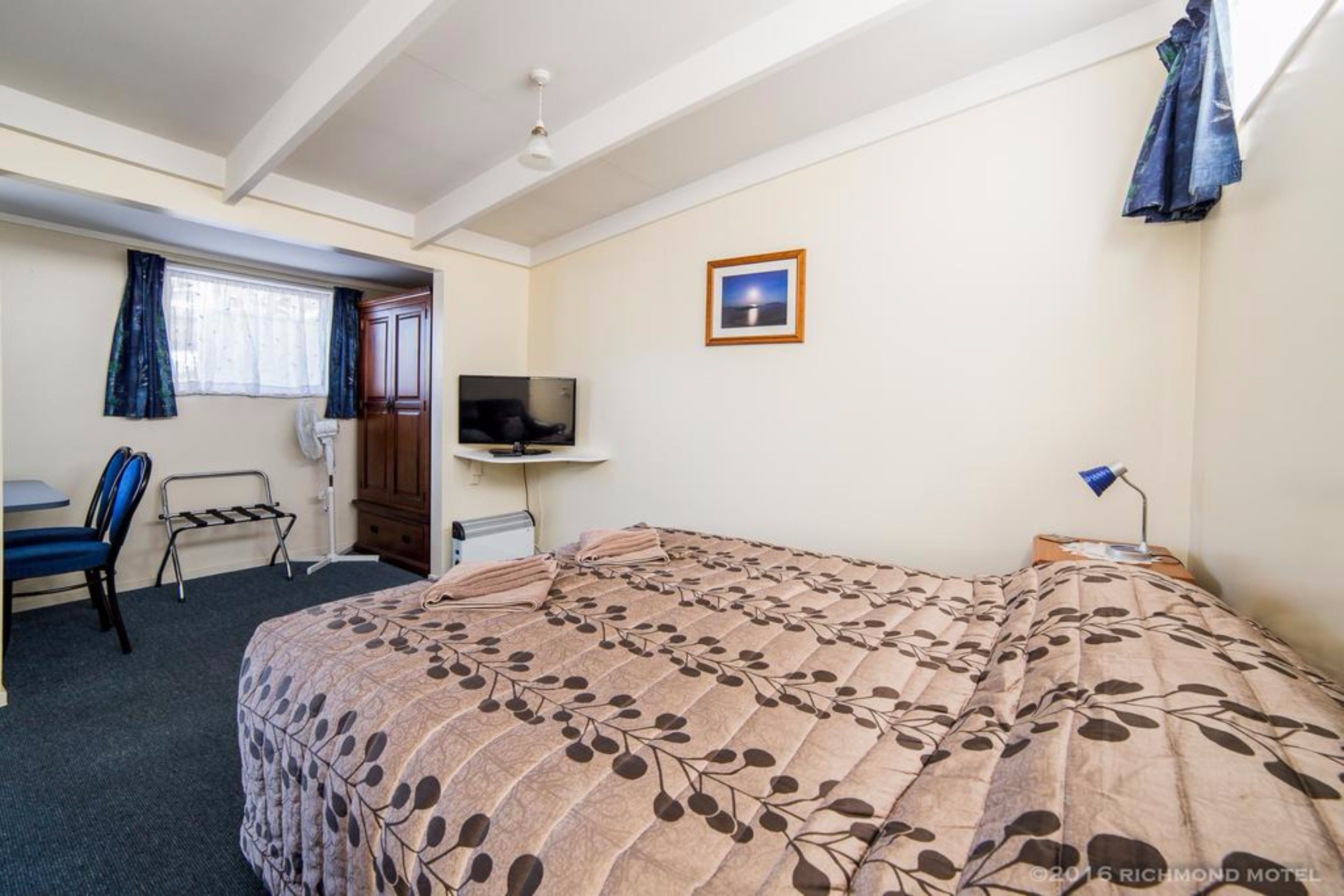 Quarto de hotel com uma cama grande, uma escrivaninha com cadeira, uma televisão e um quadro na parede.