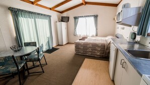 A compact room with a kitchenette, a bed, a dining area with chairs, and a television.