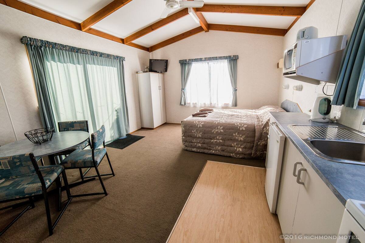 Une pièce compacte comprenant un coin cuisine, un lit, un espace repas avec des chaises et un téléviseur.