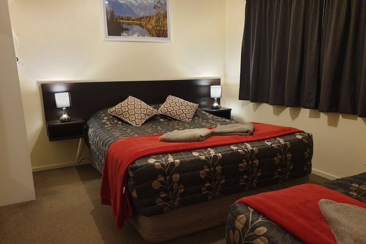 Une chambre à coucher avec un lit, deux tables de chevet, une commode, une couverture rouge et un tableau encadré accroché au mur.