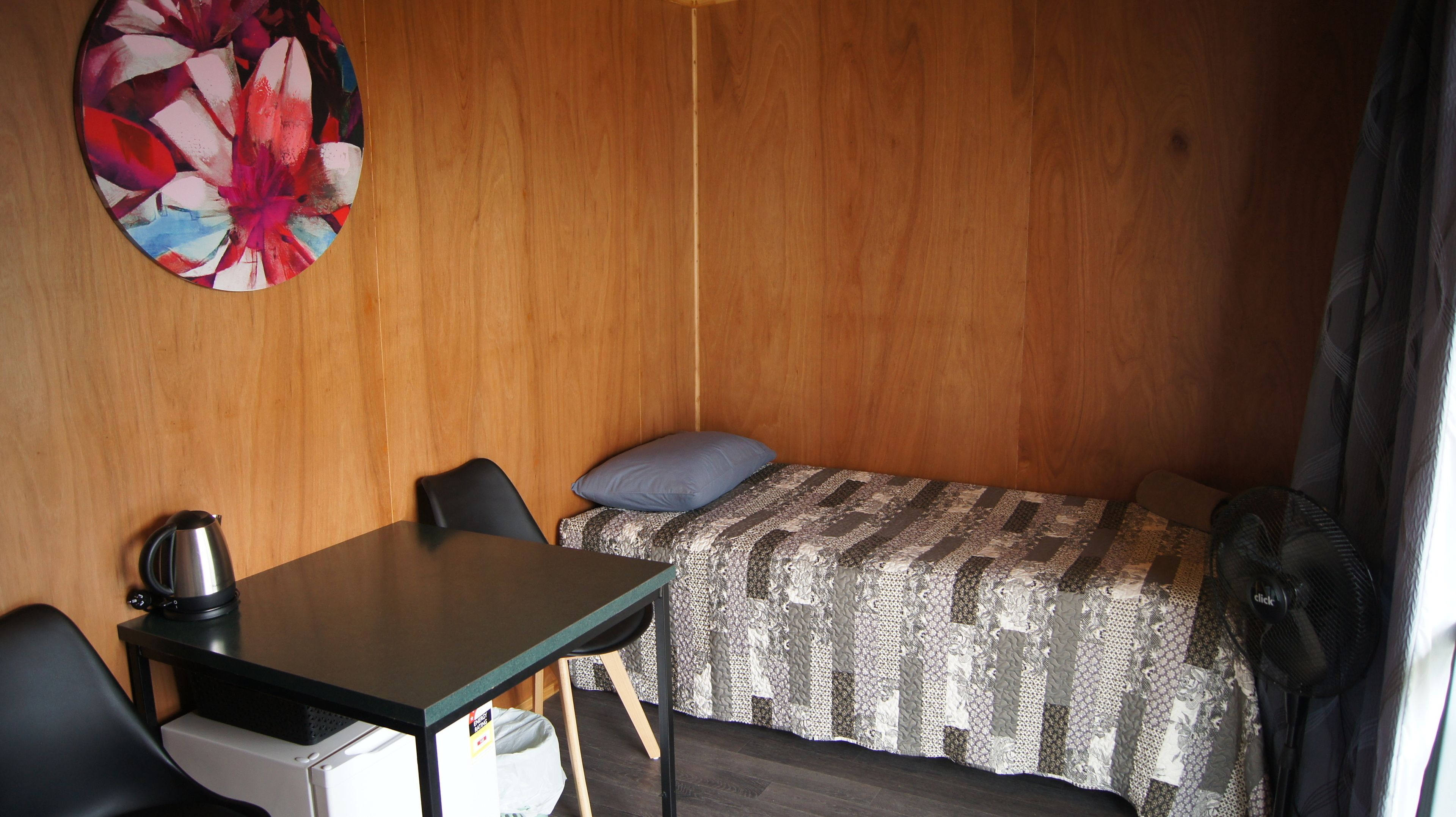 Una habitación pequeña con una cama, una mesita con un hervidor y una silla.