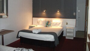 Una habitación de hotel con cama, mesita de noche, espejo y ventilador de techo.