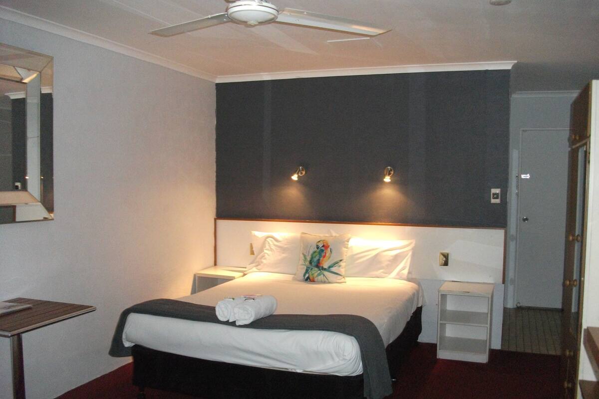 Habitació d'hotel amb un llit, una taula de nit, un mirall i un ventilador de sostre.
