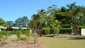 Un jardín bien cuidado con diversos árboles y arbustos, una mesa de picnic y un edificio al fondo.