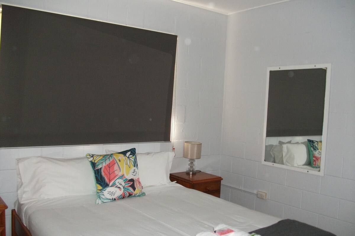 Habitació d'hotel amb un llit, una tauleta de nit, una làmpada i un mirall.