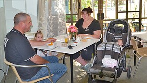 Una familia comiendo en una mesa al aire libre, con un cochecito de bebé cerca.