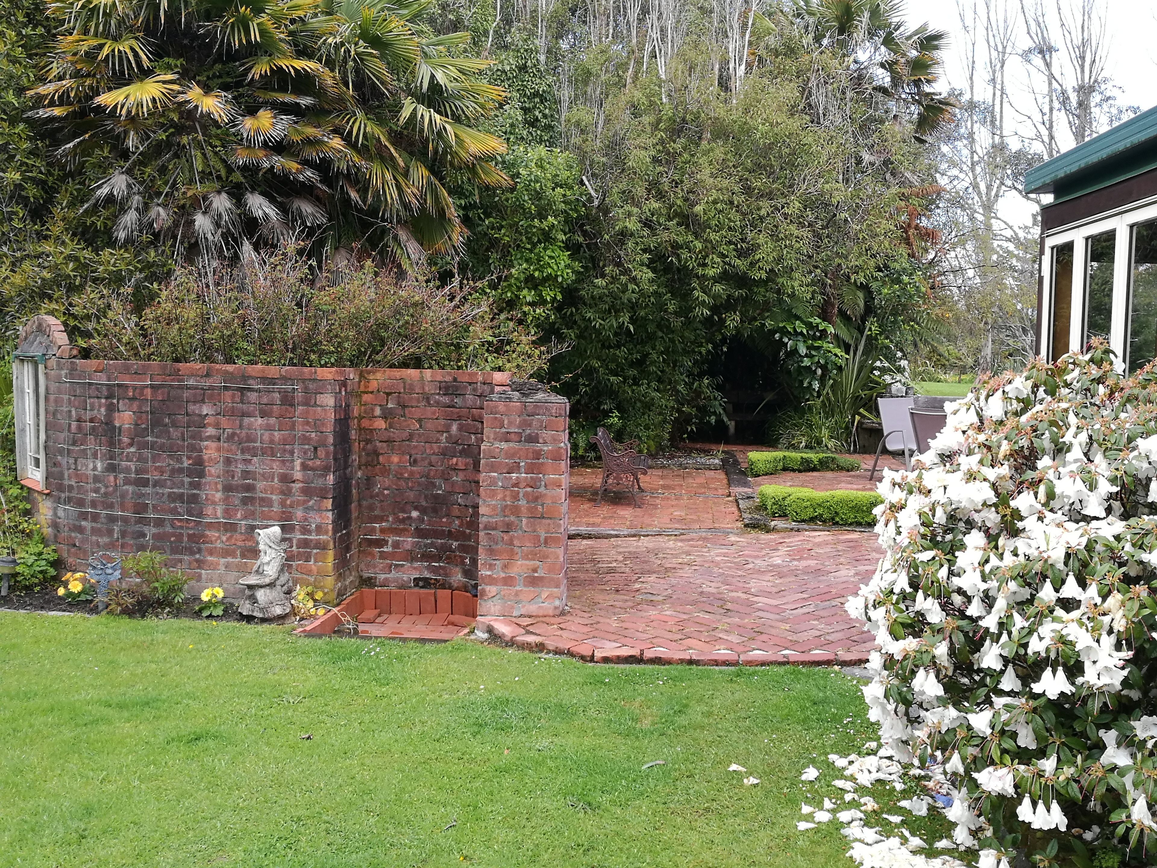 A brick pathway leading to a building with a green roof, surrounded by lush greenery and a well-maintained lawn.