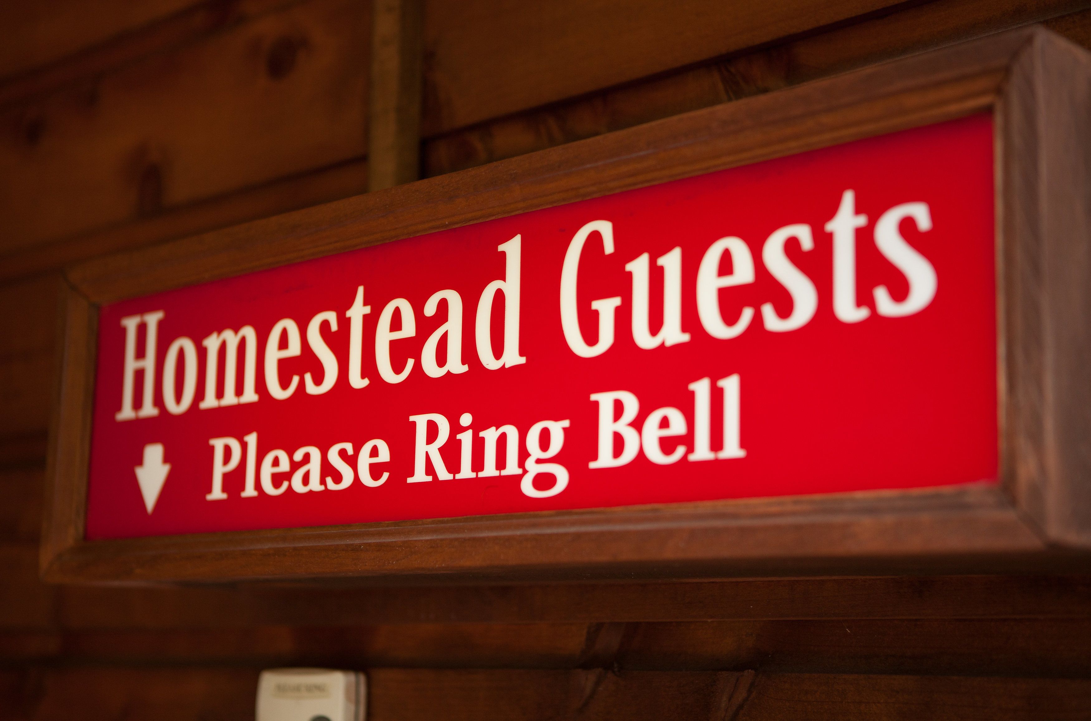 A red sign with white text that reads "Homestead Guests Please Ring Bell" and an arrow pointing downwards.