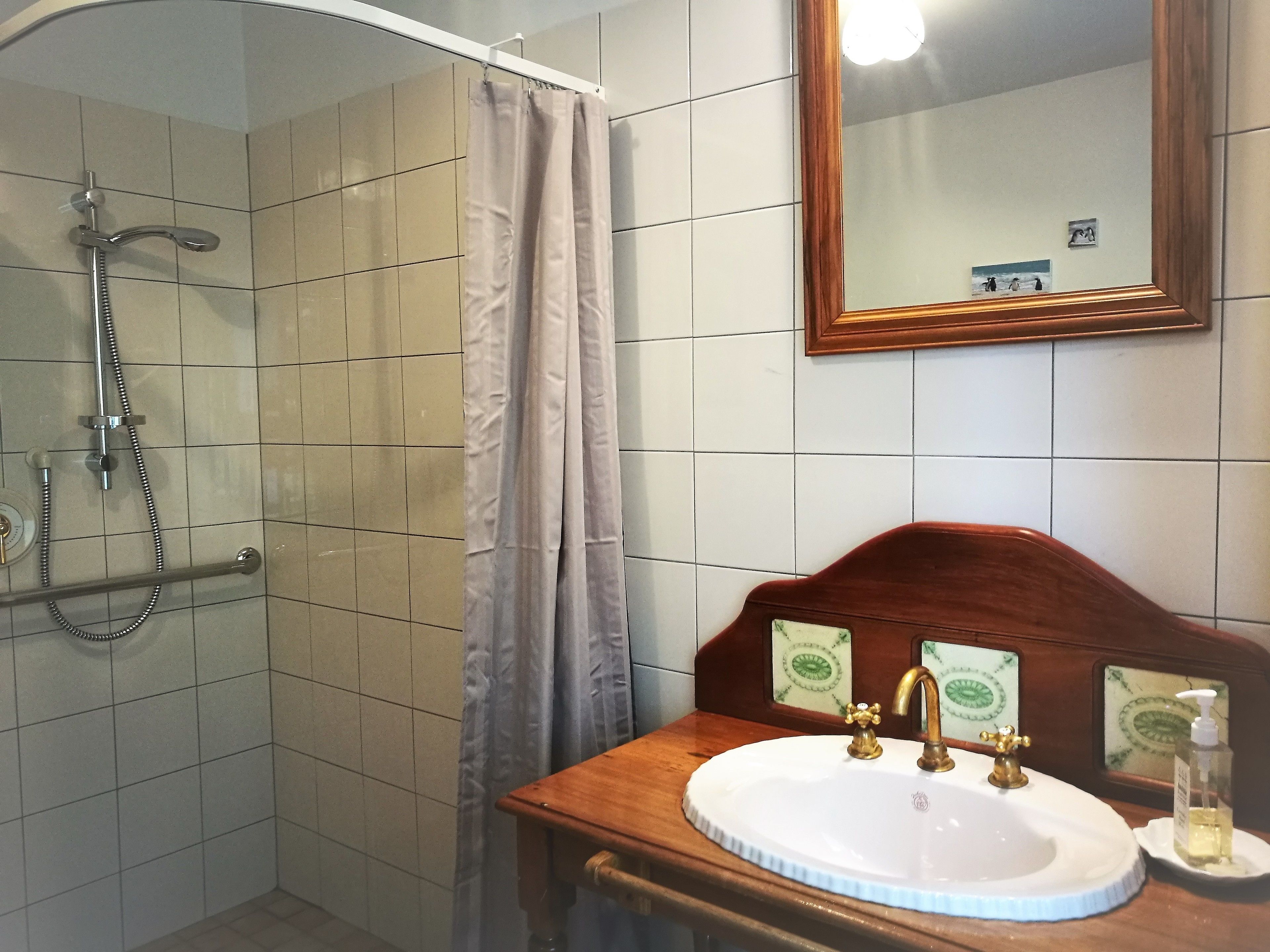 Un baño con ducha, lavabo sobre tocador de madera y espejo con marco de madera.