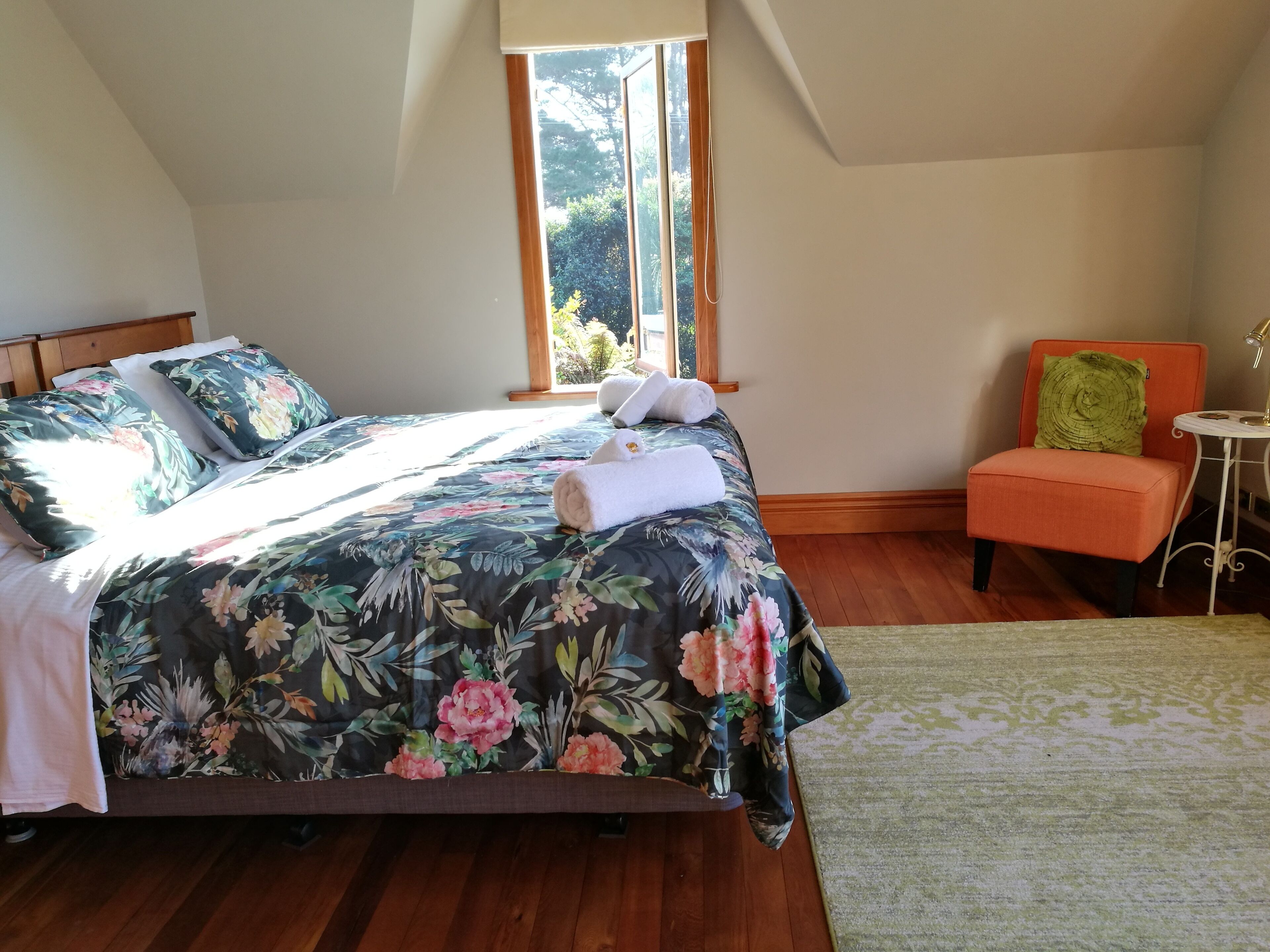 Un dormitorio con cama, una silla, un ventanal y una mesita de noche.
