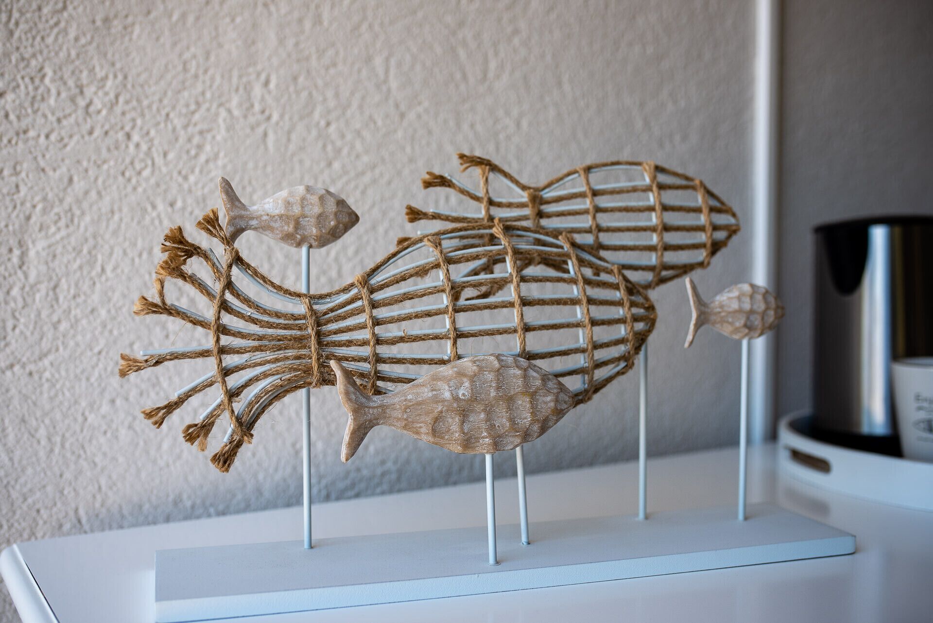 A decorative fish sculpture on a white stand against a textured wall.