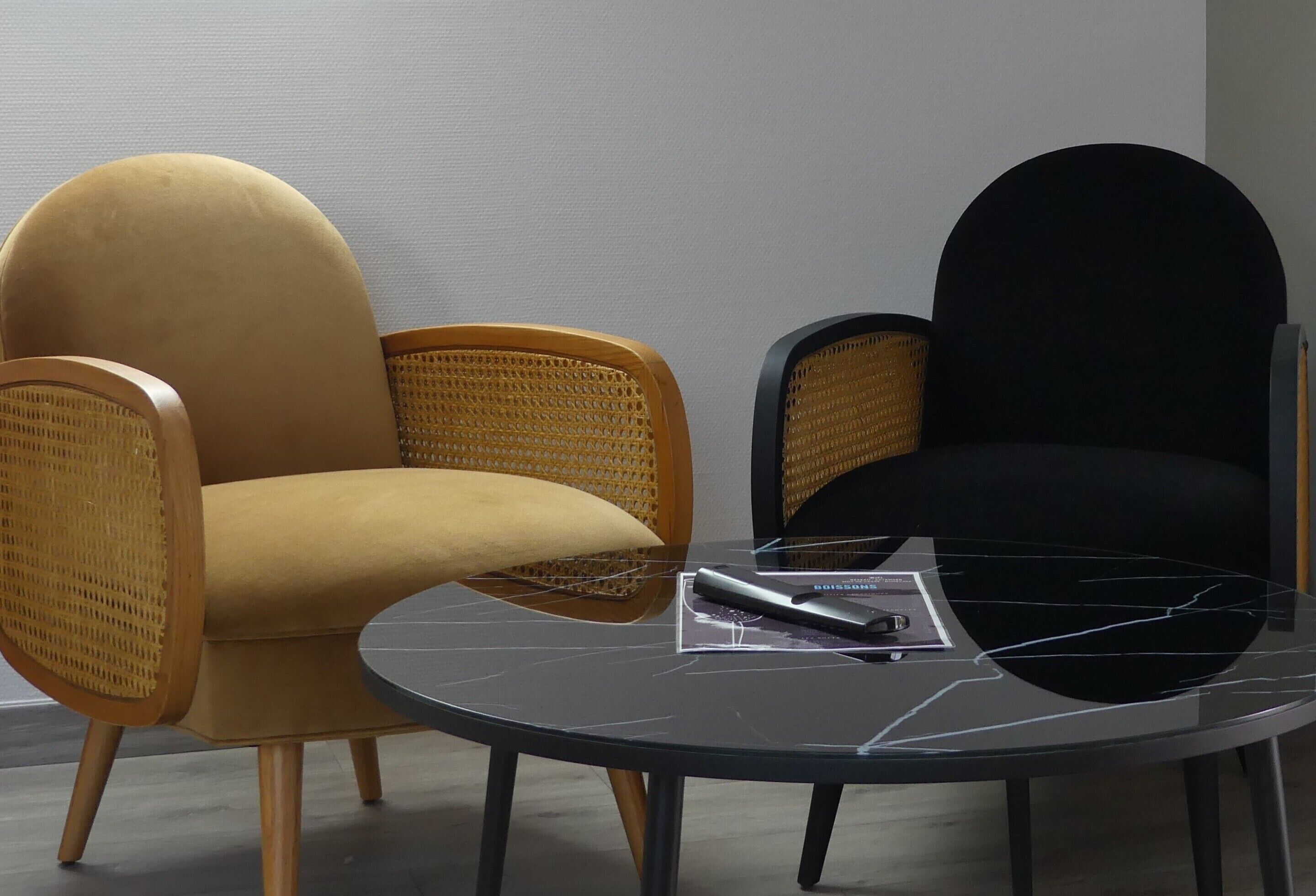 A room with two chairs, one yellow and one black, and a small table with a remote control and a magazine.