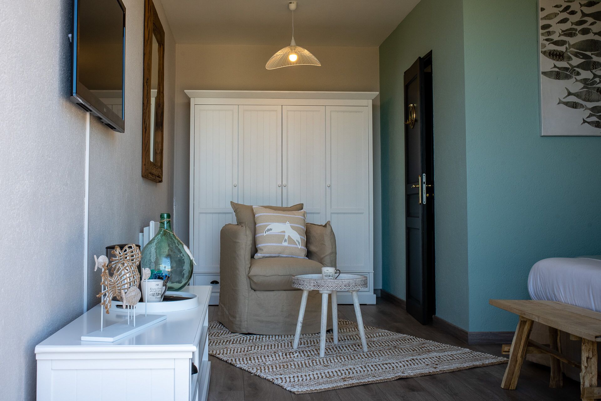 Um quarto aconchegante com um guarda-roupa branco, um sofá bege com almofadas estampadas, uma mesa redonda pequena e um tapete tecido.