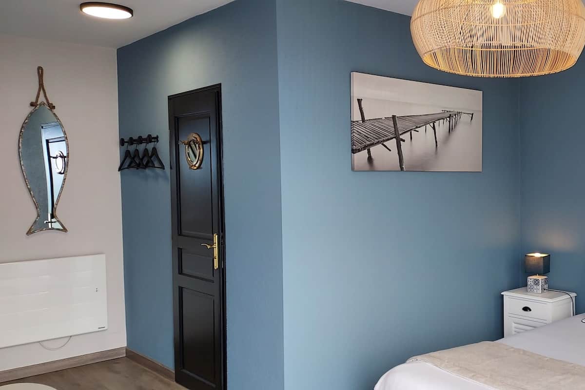 Une chambre à coucher comprenant un lit, une table de chevet, un miroir fixé au mur, un tableau et un luminaire suspendu.