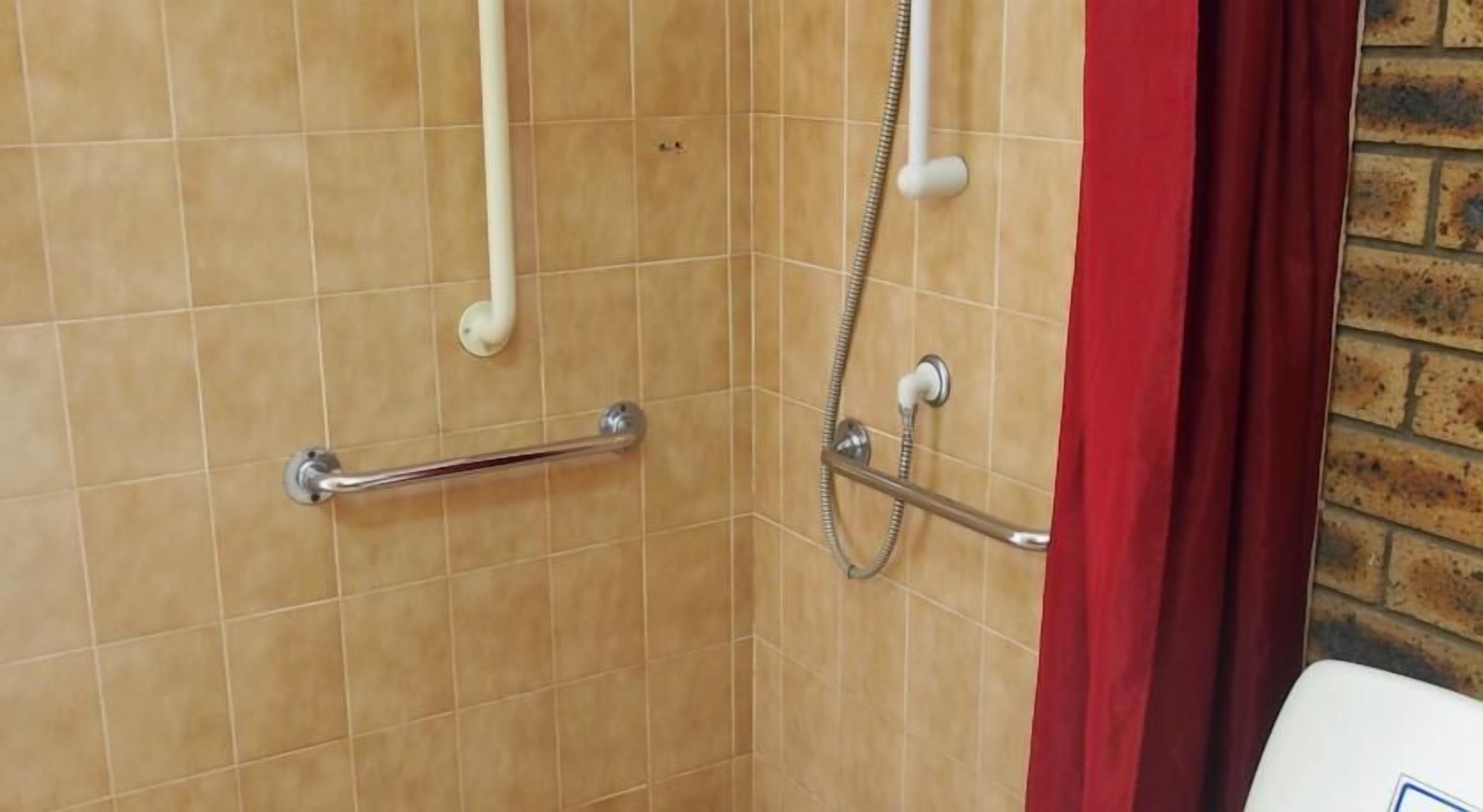 Zona de ducha con barra de apoyo, cabezal de ducha de mano y cortina roja.