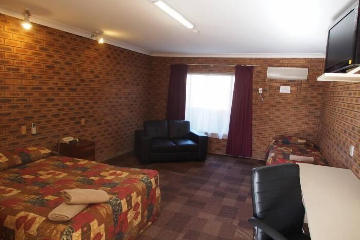 A hotel room with a brick wall, a bed with a quilt, a sofa, a desk, and a television.