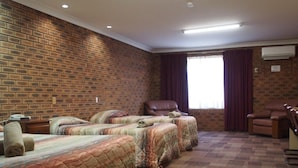 A hotel room with four beds arranged in a row, a brick wall, a large window with curtains, and an air conditioning unit.
