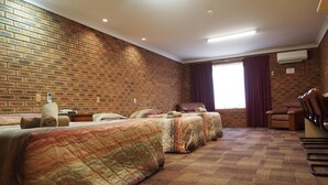 A hotel room with a brick wall, two beds with quilts, a desk, a chair, and an air conditioning unit.