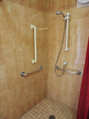 Un espace douche avec des murs carrelés, des barres d’appui et un pommeau de douche.