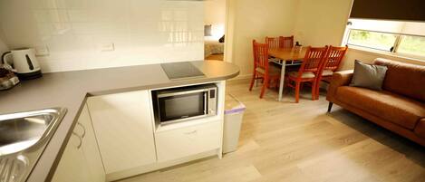A compact kitchen with white cabinets, a microwave, and a dining area with wooden chairs and a table.