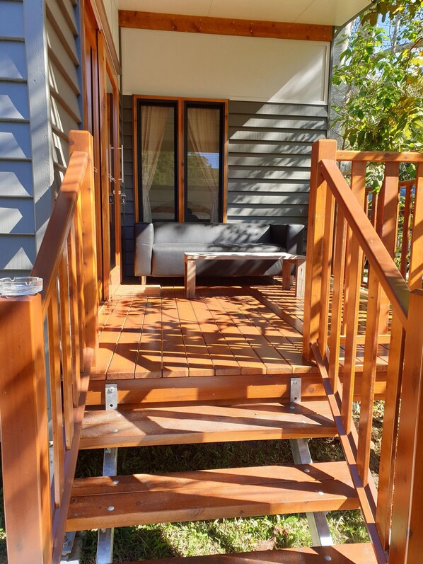 Una terraza de madera con un sofá y una mesa, que conduce a un espacio de estar cubierto con vistas al exterior.