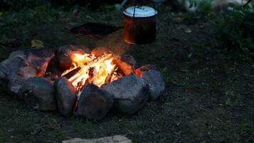 Ein Lagerfeuer mit einem darüber hängenden Topf, umgeben von Baumstämmen und Steinen.
